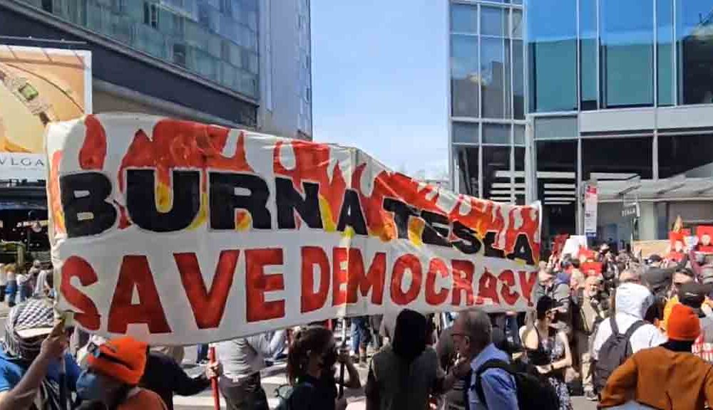 A group of people holding "Burn a Tesla" banner outside the Manhattan Tesla showroom