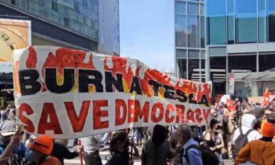 A group of people holding "Burn a Tesla" banner outside the Manhattan Tesla showroom
